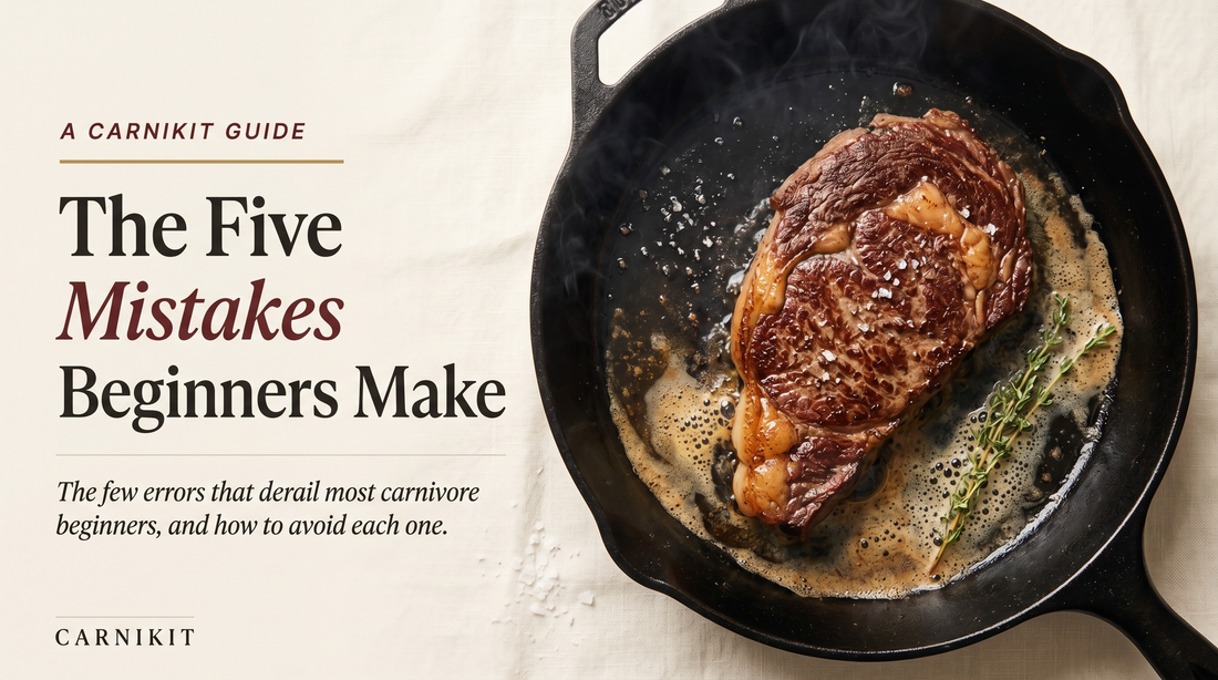 Editorial overhead photograph of a marbled ribeye steak searing in foaming butter in a black cast-iron skillet, with a sprig of thyme and a scatter of sea salt, on cream linen — the cover image for Carnikit's guide to common carnivore diet mistakes.