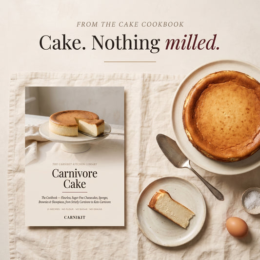 Book cover for 'Carnivore Cake' by Carnikit, styled in a warm flat-lay composition alongside a baked cake, a slice of cake on a plate, an egg, and a spoon on a textured cream fabric background.
