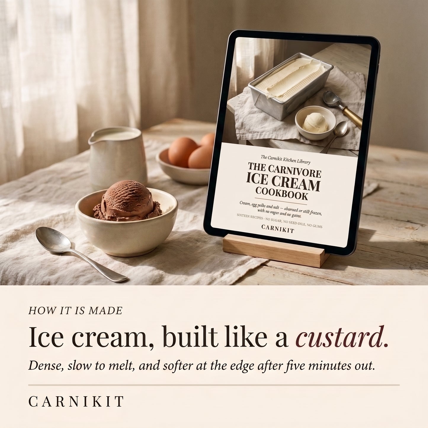 A tablet on a wooden stand displays the cover of 'The Carnivore Ice Cream Cookbook' by Carnikit. The scene is styled on a rustic table with a bowl of ice cream, eggs, a small pitcher, and a spoon, under warm natural light.